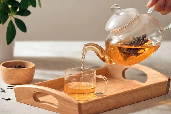 木製のサービングの皿のガラスティーポットからお茶を注ぐ手 — ストック写真