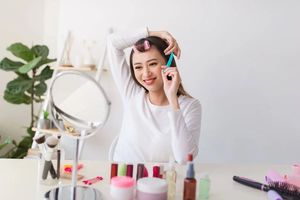 Hairstyle tutorial. Asian woman brushing her hair and smiling pleasantly while filming a tutorial for her beauty blog