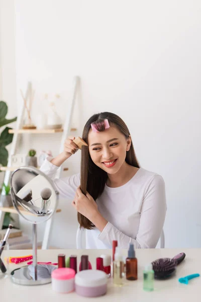 Hairstyle tutorial. Asian woman brushing her hair and smiling pleasantly while filming a tutorial for her beauty blog