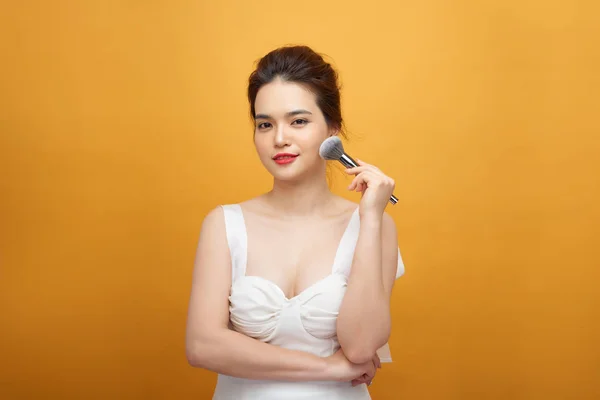 beautiful woman holding makeup brush over yellow