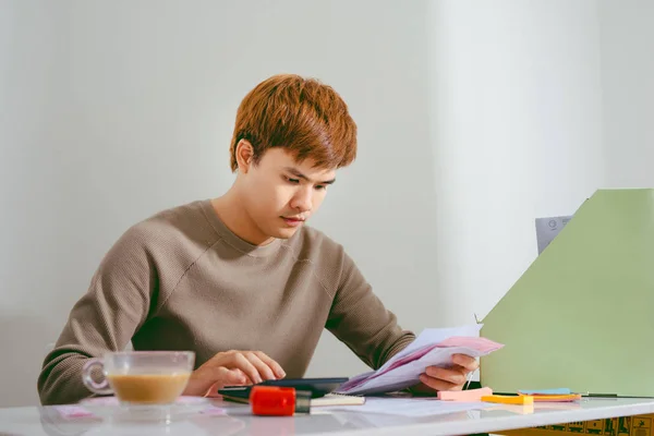 Stressed asian man working through paperwork, calculating expenses, trying to save some money, managing finances, sitting at table with laptop, trying to make finance plan
