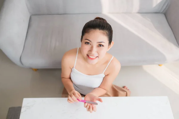 Attractive Asian woman correcting fingernail using nail fail, sitting at table