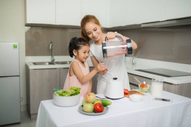 Anne ve kızı salatayı blender menüsünde hazırlıyorlar. Lezzetli smoothie ve evdeki masada malzemeler var.