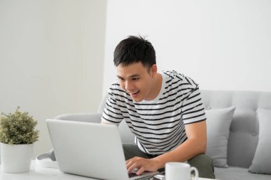 Genç yakışıklı adam oturma odasında dizüstü bilgisayar ile oturan ve gülümseyen