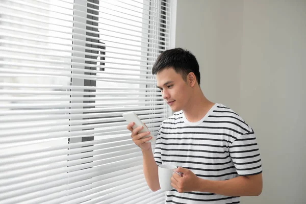 Sonriente Joven Guapo Usando Teléfono Junto Ventana — Foto de Stock