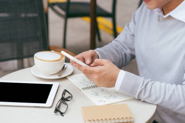Yakışıklı genç beyaz adam kafede cep telefonu kullanarak oturan ve kahve içiyor. Kahve fincan ve onun akıllı telefonda metin mesajı okuma ile Asyalı erkek.