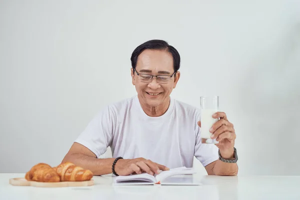 Anciano Bebiendo Leche Leyendo Libro Mientras Desayuna — Foto de Stock