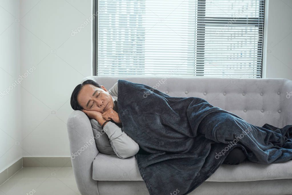 Male pensioner sleeping on couch, suffering from high temperature, disease