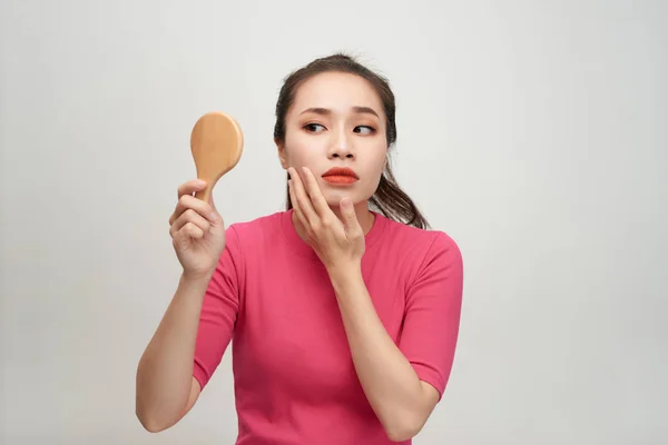 Woman holding a mirror, touch and worrying about her face