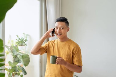 Genç adam cep telefonu üzerinde konuşurken evde penceresine bakarak gülen