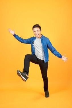 Turuncu arka plan üzerinden atlama t-shirt giymiş Neşeli genç Asyalı adam kazanan jest yapmak.