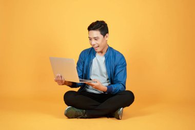 Heyecanlı mutlu asyalı adam dizüstü bilgisayar ekranına bakarak ve başarı renk arka plan üzerinde izole kutluyor