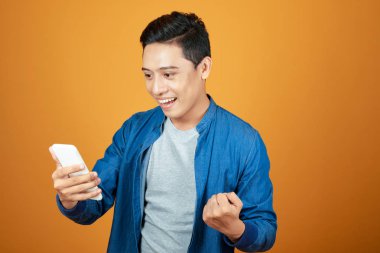 Başarı ya da başarı kutlamak için onun smartphone vasıl seyir ve kolunu kadar yükselterek mutlu heyecanlı Asyalı adam.