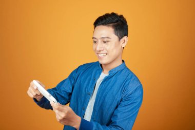 Genç Asyalı adam portre cep telefonu video oyunu oynarken. Turuncu arka planda.