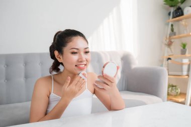 Güzel genç Asyalı kadın yüzünde makyaj için temel uygulamak için güzellik blender kullanarak.