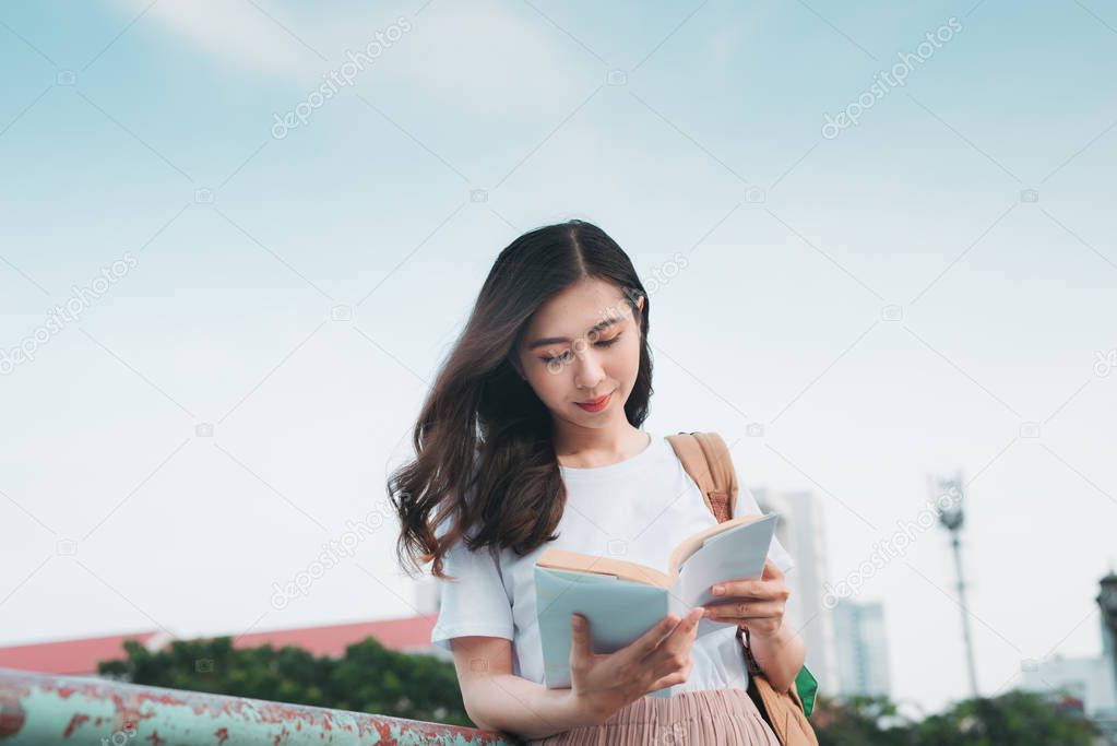Asian Business Woman traveling, standing by railing bridge, reading book on city background.