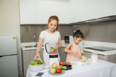 Genç Asyalı anne ve kız taze sıkılmış domates püresi yapıyor, kızı çok mutlu.