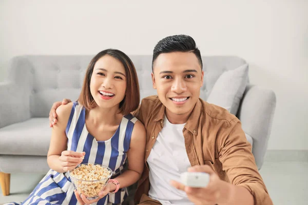 Shot of a cheeful young Asian couple watching television at home