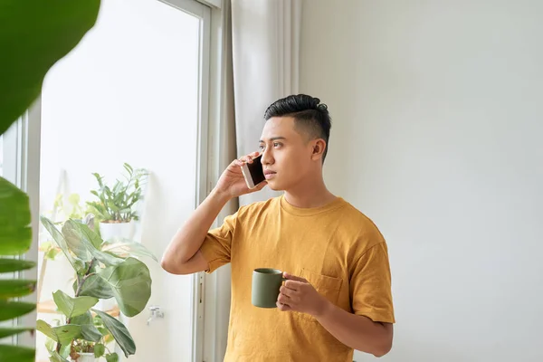 Улыбающийся Молодой Человек Разговаривает Мобильному Телефону Смотрит Окно Дома — стоковое фото