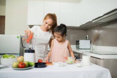 Genç Asyalı anne ve kız taze sıkılmış domates püresi yapıyor, kızı çok mutlu.