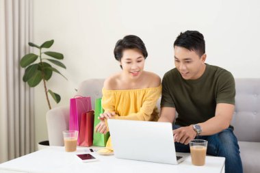 Çevrimiçi mağazaları izleyen mutlu genç Asyalı çift evde bilgisayar satın alıyorlar..