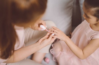 Güzel, genç Asyalı anne, küçük tatlı kızına oje sürüyor..
