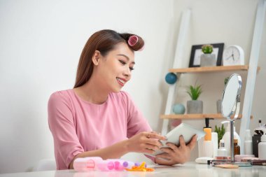 Evde tablet kullanarak saç curlers giyen mutlu Asyalı kadın