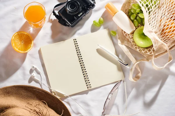Picnic concept. Hat, sun cream, fruit bag, juice, notebook, camera and sun cream on white background.