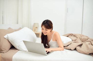 Evde dizüstü bilgisayar kullanan gülümseyen Asyalı genç kadın.