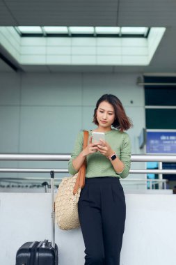 Asya 'da havaalanında bekleyen Asyalı kadın akıllı telefonunu kontrol ediyor..