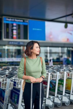 Havaalanında otobüsünü beklerken elinde bavuluyla Asyalı genç bir kadın..