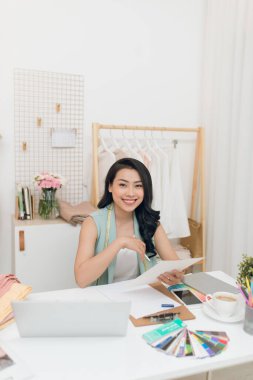 Moda tasarımcısı iş başında. Mutlu genç Asyalı kadın moda atölyesinde onu iş yerinde otururken çizim