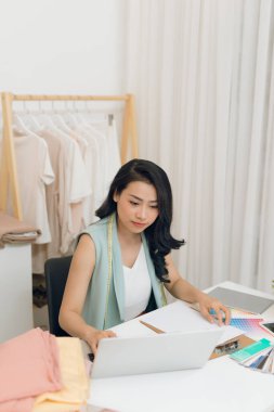 Genç bir Asyalı moda tasarımcısı atölyesinde dizüstü bilgisayarla çalışıyor.