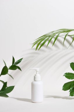 Beyaz arka planda izole edilmiş tropikal yapraklı boş bir kozmetik şişe.