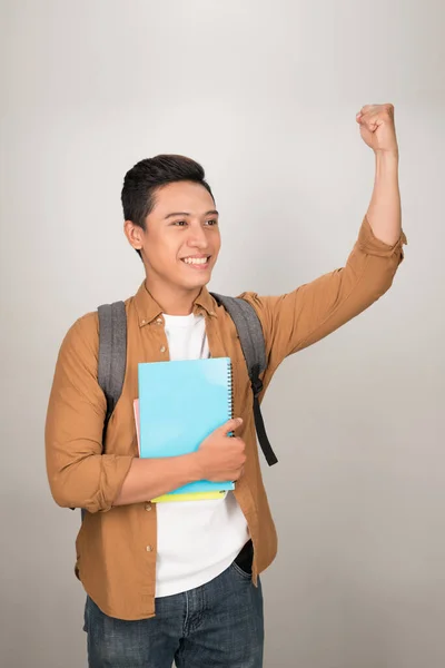 A young Asian student feeling excited and carrying his backpack and books isolated on a white background.