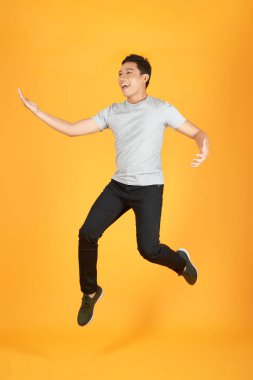 Turuncu arka plan üzerinde izole başarı kutlarken beyaz t-shirt atlama heyecanlı bir genç adamın tam uzunlukta portre