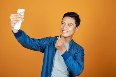 Renkli turuncu arka planda akıllı telefon ile genç mutlu Asyalı adam selfie