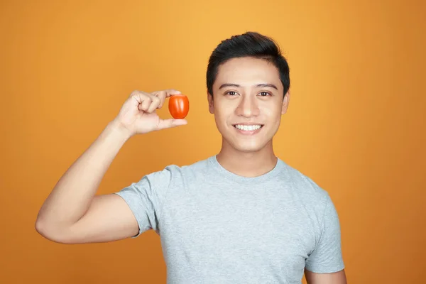 Junger Asiatischer Mann Hält Eine Tomate Auf Orangefarbenem Hintergrund — Stockfoto