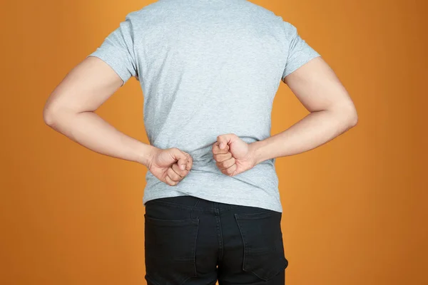 Men with low back pain on a color orange background / medical and health concepts.
