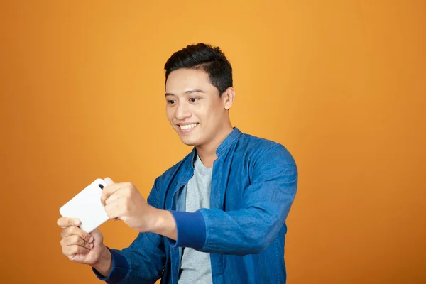 Молодой Азиат Играющий Видеоигры Мобильном Телефоне Оранжевом Фоне — стоковое фото