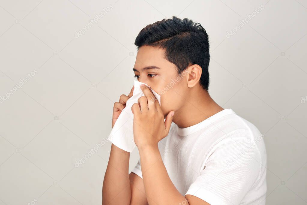 Closeup of sick Asian man blowing nose into tissue, suffering from common cold. Medical and healthcare concept on white background