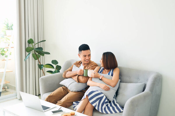 Счастливая молодая азиатская пара отдыхает на диване по утрам и пьет вместе
. 