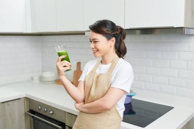 Detox konsepti. Asyalı kızın ev yapımı yeşil meyve suyu bardağıyla portresi. Boş alana bakıyor.