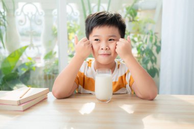 Bir bardak sütle masada oturan tatlı çocuk.