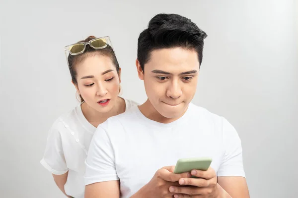 Photo of couple with her looking into her guy screen and him cheating to his lover smiling isolated over white background