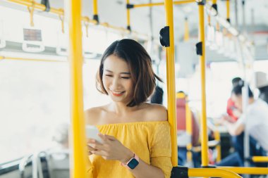 Telefon kullanan ve otobüs / toplu taşımada duran Asyalı genç kadının portresi.