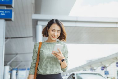 Genç iş kadını dışarıda beklerken uçağını kontrol etmek için telefon kullanıyor..