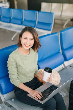 Kahve zamanı. Havaalanı salonunda oturan, kahve içen ve dizüstü bilgisayarla çalışan çekici bir kadın.