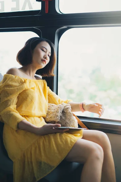 Young Asian woman sleeping on the bus while her hand holding the tablet.