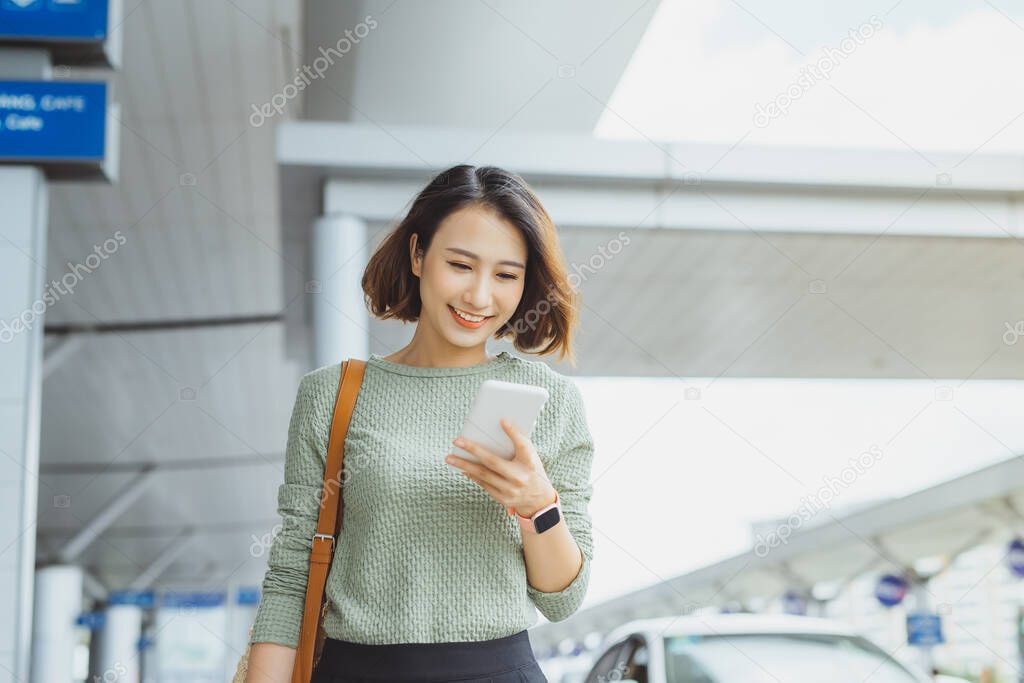 Young businesswoman using phone to check her flight when standing outside.